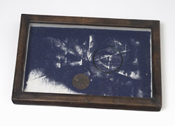 A dark wooden frame containing  dark blue sand which pours over a white background