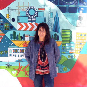 A woman with brown hair and a purple shirt standing in front of a colorful backdrop