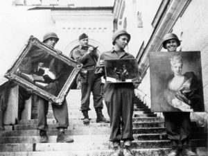 A black and white photograph showing men in army uniforms holding paintings