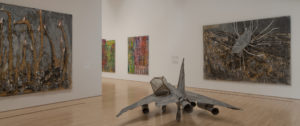A sculpture of a plane in a gallery between two abstract paintings
