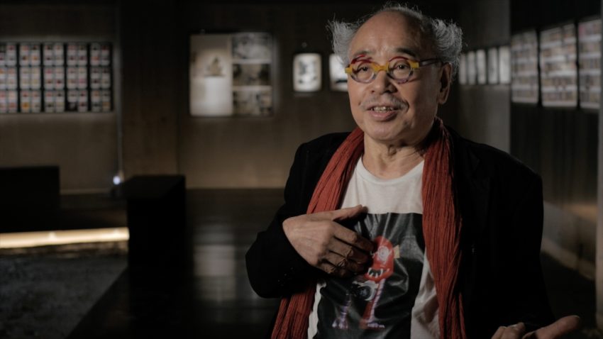 Photographer Nobuyoshi Araki in a photo gallery, wearing a shirt with a monster on it