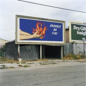 A color photograph of a large blue and orange billboard with the words "oranges on fire", Mandel Sultan