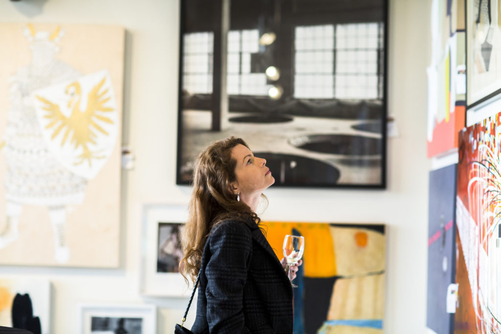 A woman stands in a room surrounded by a wide variety of paintings and photographs.
