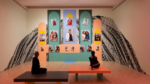 Two people sitting on benches inside of an SFMOMA gallery staring up at an artwork installation by artist Marcel Pardo Ariza.